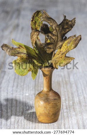 Small wooden vase with autumn leaf. White wooden background