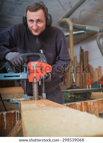 Close up of a smiling Carpenter who is mill-cutting a wooden board with chain mortiser. He is wearing soundproofing headphones