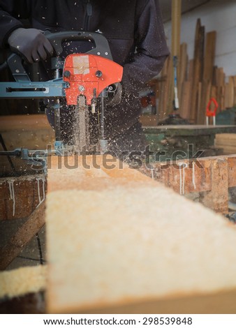 Close-up of the hands of a man with chain mortiser mill-cutting a wooden board