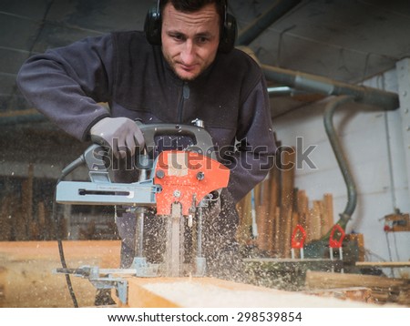 Close up of a Carpenter who is mill-cutting a wooden board with chain mortiser. He is wearing soundproofing headphones