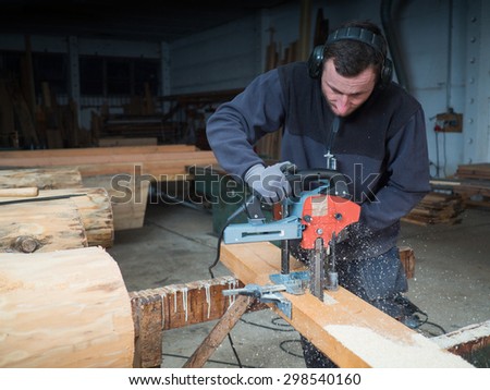 Close up of a Carpenter who is mill-cutting a wooden board with chain mortiser. He is wearing soundproofing headphones