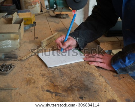 Close up of the hands of a carpenters drawing with a blue pencil on a sheet of paper
