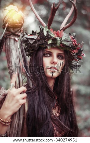 portrait of a beautiful brunette with a painted face, clothes shaman, a floral wreath on her head and horns, holding a glowing wooden staff, in the woods