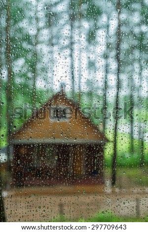 Wet glass with raindrops. In the background part of Ã?Â�ountry house in the woods. Focus on raindrops