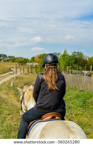 closeup of a back view of a young woman on horseback at the countryside - focus on the head