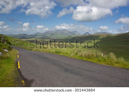 Pastoral landscape showing road and fields Ring of Kerry on west coast of Ireland near the mountains on a sunny day with green fields and blue skies with clouds and mountains.