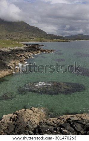 Afternoon coastal farm scene on the west coast of Ireland with light shining through broken storm clouds and clear sea and sandy beaches during stormy weather in summer in county Mayo.
