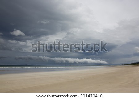 Landscape  scene on the west coast of Ireland with dramatic broken storm clouds and blue sky over rocks on a deserted sandy beach during stormy weather in summer in county Kerry.