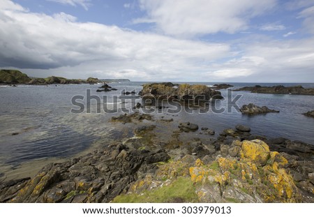 Coastal rocky landscape showing rocky  beaches and cliffs in County Antrim in the UK on the Atlantic north west coast of Ireland on a sunny day with  blue skies with clouds and mountains.