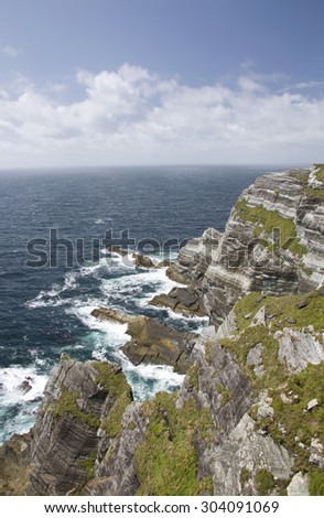 Scene on the ring of Kerry on the Atlantic west coast of Ireland with waves breaking dramatically at the foot of high cliffs on a rocky coast during stormy weather in summer in county Kerry.