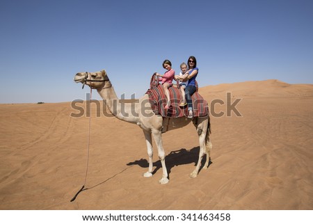 Western female tourist, a mother on holiday with her two children, enjoying a camel ride together in the desert in the United Arab Emirates