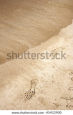 Golden sand background just brushed by a wave with human foot print