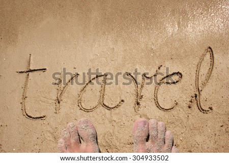 Travel hand written in sand on a beach on an exotic island background with feet metaphor for summer, ocean, sea, travel, vacation, tourism, tropical, coast, message, resort, paradise, sunny or water