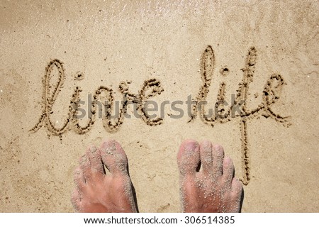 Conceptual live life handwritten in sand for natural, symbol, tourism or concept designs background with feet