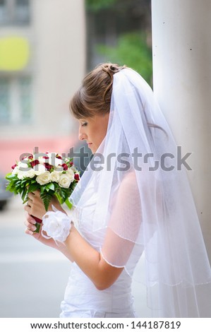 pensive bride in white dress standing and holding roses bouquet