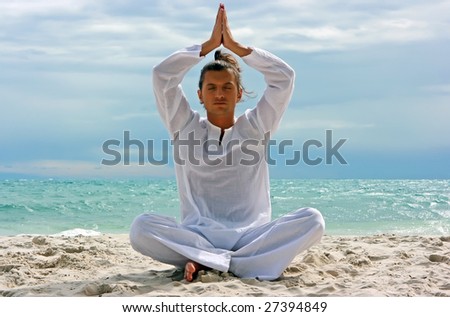 Young man practising yoga on the sandy beach