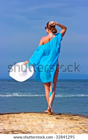 Brunette lady in blue shawl and white hat standing on the rocky beach