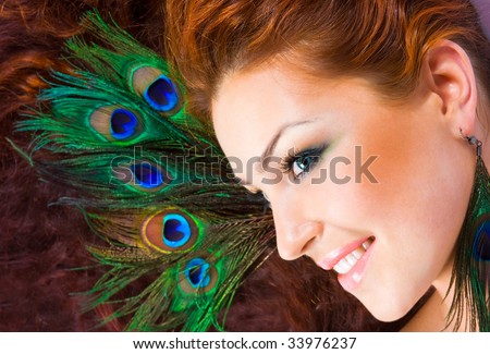 Close-up beautiful luxury red-hared model with perfect make-up with peacock feather in her hair and peacock earrings