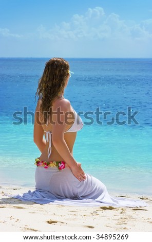 Beautiful brunette with long hair sitting on the sand beach in Indonesia and turned her back to us
