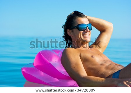 Handsome muscular young man floating on inflatable raft in sea water