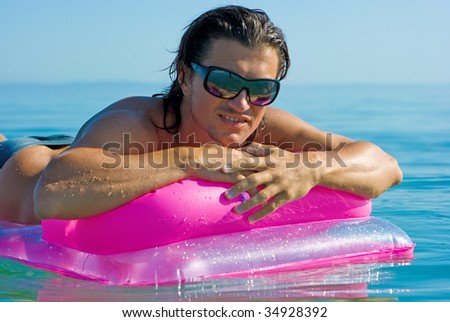 Handsome muscular young man floating on inflatable raft in sea water