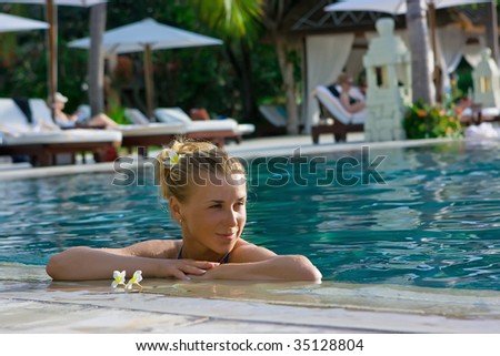 Beautiful blonde girl in hotel swimming pool with flower in long hair