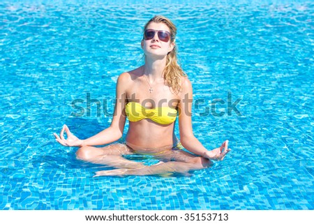 Beautiful blonde yoga girl making excercise in the swimming pool