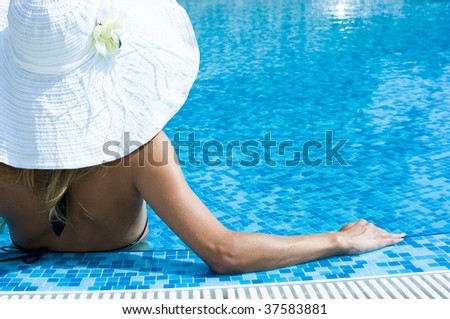 Blonde girl in white hat sitting in swimming pool