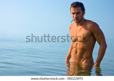 Male athlete with very muscular figure standing in sea water