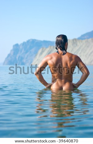 Male athlete with very muscular figure standing in sea water and looking at mountains