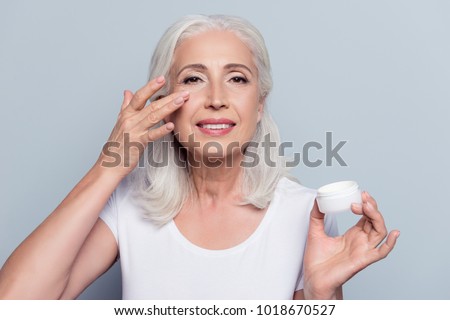 Perfect, pretty, woman applying eye cream, holding jar of cosmetic product looking at camera over gray background