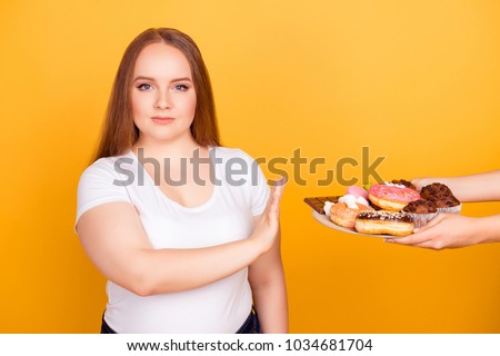 I\'m against eating products containing fat! Will-powered woman wearing white tshirt is refusing to consume tasty delicious sweets on a plate, isolated on bright yellow background