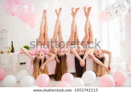 Charming pretty cheerful foolish attractive sexy stylish slender girls lying head over heels on bed with raised crossed legs hands celebrating birthday holiday event looking at camera  sleepover party