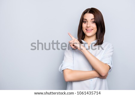 Portrait with copy space of charming, pretty, nice, stylish, brunette, trendy woman in shirt with modern hairstyle, pointing  forefinger on empty place, looking at camera, isolated on grey background