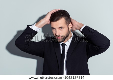 Stunning, perfect, manly, virile, harsh guy in classic outfit holding two hands on head, looking to the side with serious expression, isolated on grey background