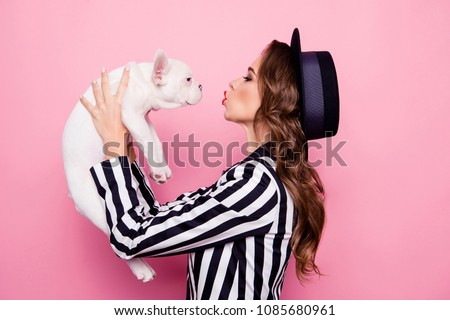 Side view, half face, profile portrait of attractive, pretty, charming girl raise dog in front of face, blowing kiss to pet, isolated on pink background