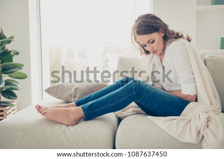 Sad, upset, unhappy woman holding hands on stomach suffering from abdominal pain with close eyes, having menstrual period, food poisoning, gastritis, diarrhea, feeling unwell sitting in livingroom