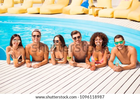 Six international hot teens students in diverse swim wear and spectacles are chatting in the pool, sunshine, blue sky, drinks are on white wooden floor, holiday together on beach resort