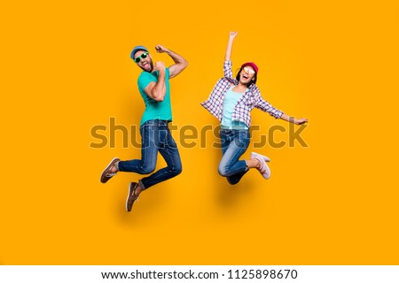 Portrait of funky active couple jumping with raised fists celebrating victory wearing casual clothes isolated on vivid yellow background