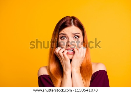 Portrait of red straight-haired attractive cute nice scared worried young girl, biting nails. Isolated over bright vivid yellow background