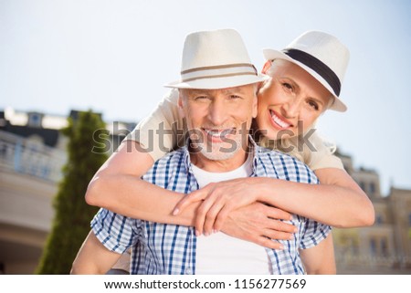 He vs she together forever! Portrait of cheerful positive grandma and granddad in straw hats, attractive man carrying on back charming woman, enjoying time together outdoor