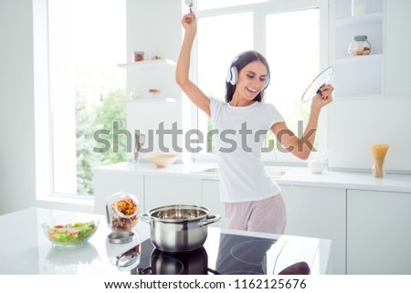 Adorable nice charming cheerful pretty beautiful stylish excited girl listening to music, singing in modern light white kitchen, cooking homemade dish with domestic products