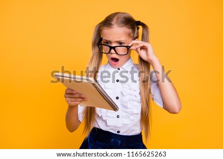 What is it! I do not understand it! Close up photo portrait of sad angry annoyed upset schoolkid with open mouth adjusting glasses staring looking at copybook textbook isolated bright background