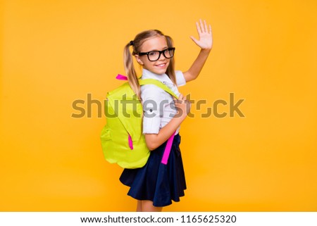 Photo of small girl turned around half a turn and waving hand look at camera isolated on bright yellow background with copy space for text
