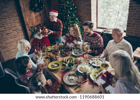 Top above high angle view of noel gathering, meeting. Adorable large  grandparent in headwear giving away, changing gifts sister brother son daughter at feast lunch table fun joy bag sack