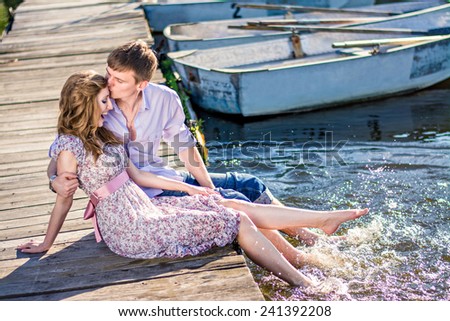 couple in love  sitting on a wooden pier near the boat. Man and woman kiss on the dock, down feet in the water.