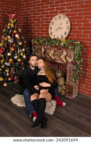 on Christmas Day, sitting by the fireplace near the Christmas tree pregnant young wife laid her head on shoulder her loved. man hugging his beloved