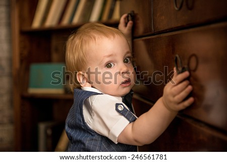 Cute little boy holding the handle of the drawer on the background of the bookcase