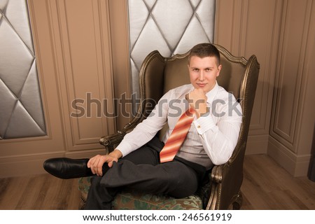 Thoughtful businessman in chic interior. thoughtful young man in a business suit sitting on the armchair with his legs crossed and keeps his hand on his chin