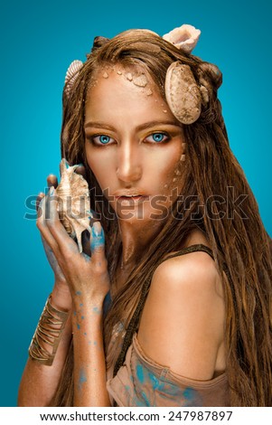 sound of the sea in a shell. beautiful girl with creative make-up holding a shell and looking at the camera